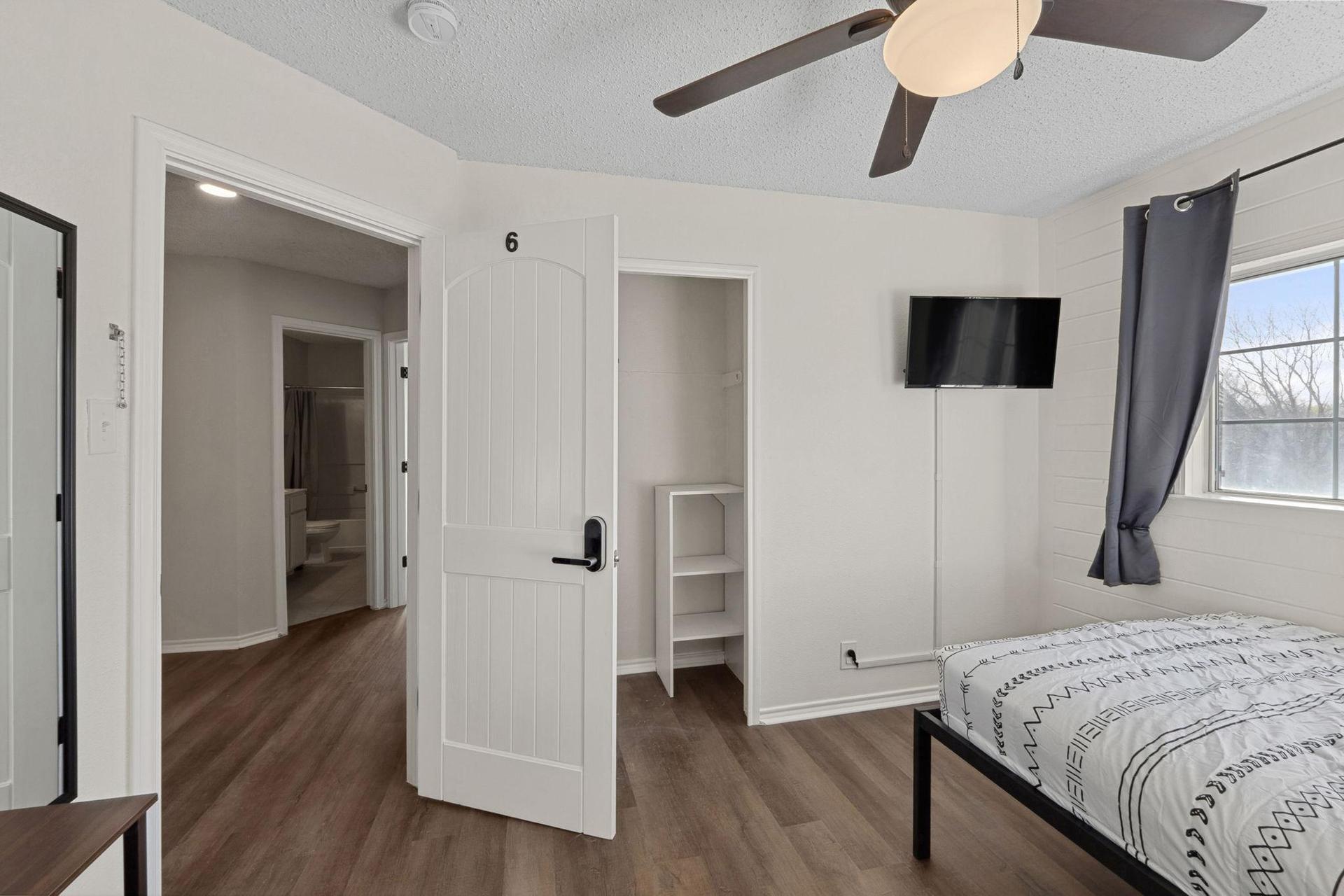 Bedroom with comfortable bed, a mini fridge, a TV, and a work desk. A closet & a ceiling fan.