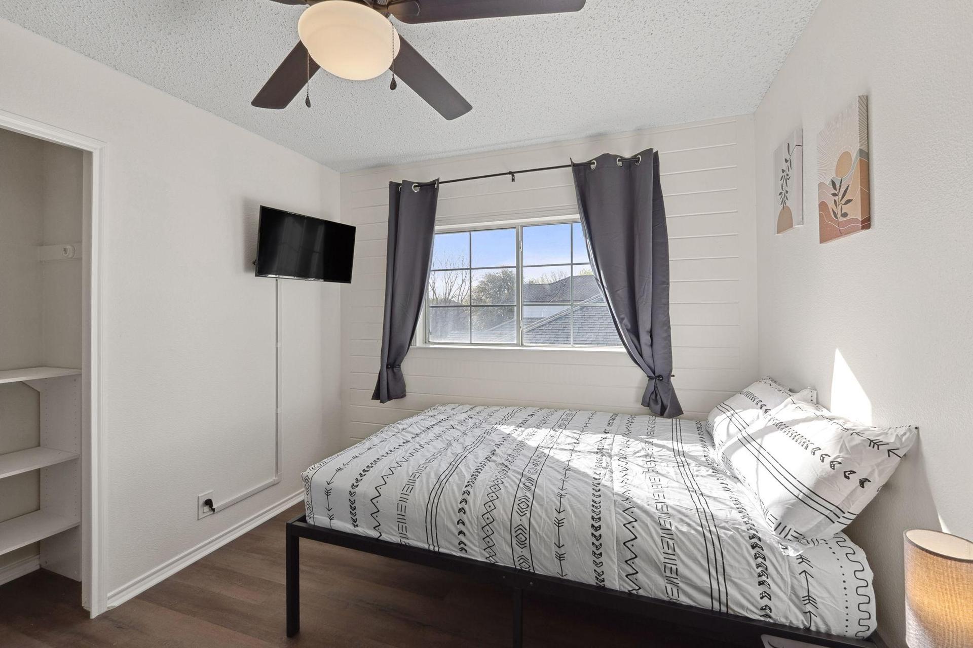 Bedroom with comfortable bed, a mini fridge, a TV, and a work desk. A closet & a ceiling fan.