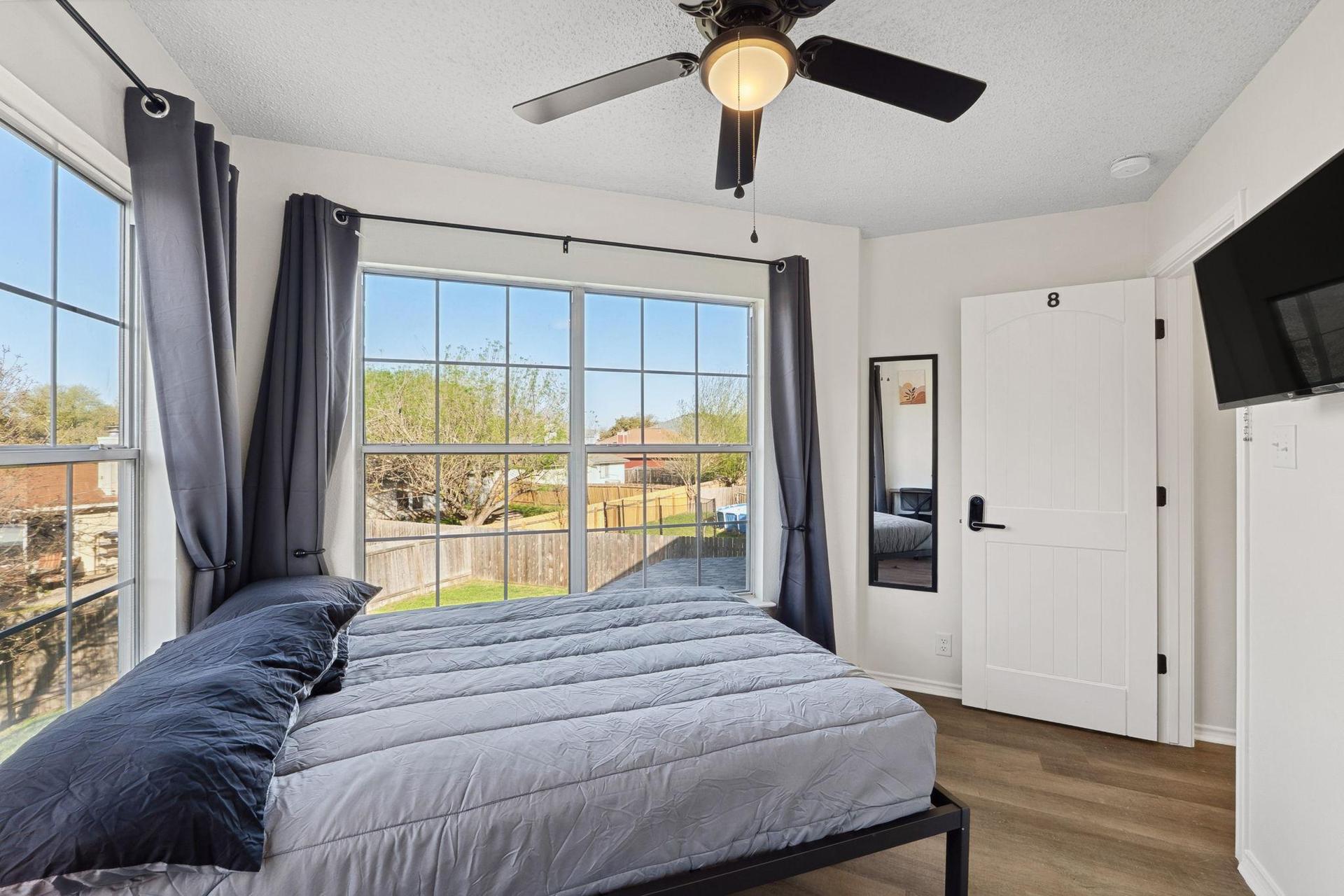 Bedroom with comfortable bed, a mini fridge, a TV, and a work desk. A mini closet & a ceiling fan.