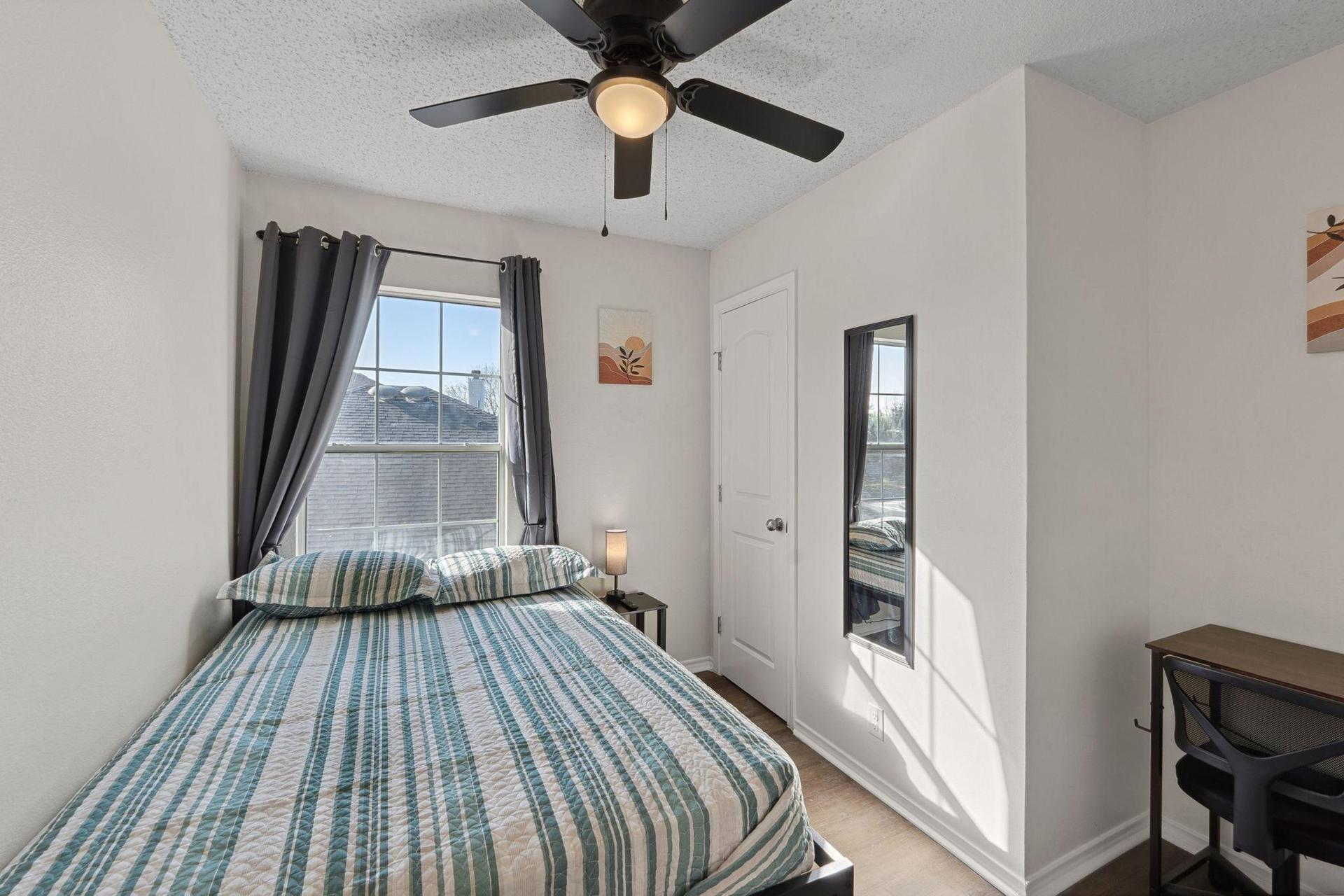 Bedroom with comfortable bed, a mini fridge, a TV, and a work desk. A mini closet & a ceiling fan.