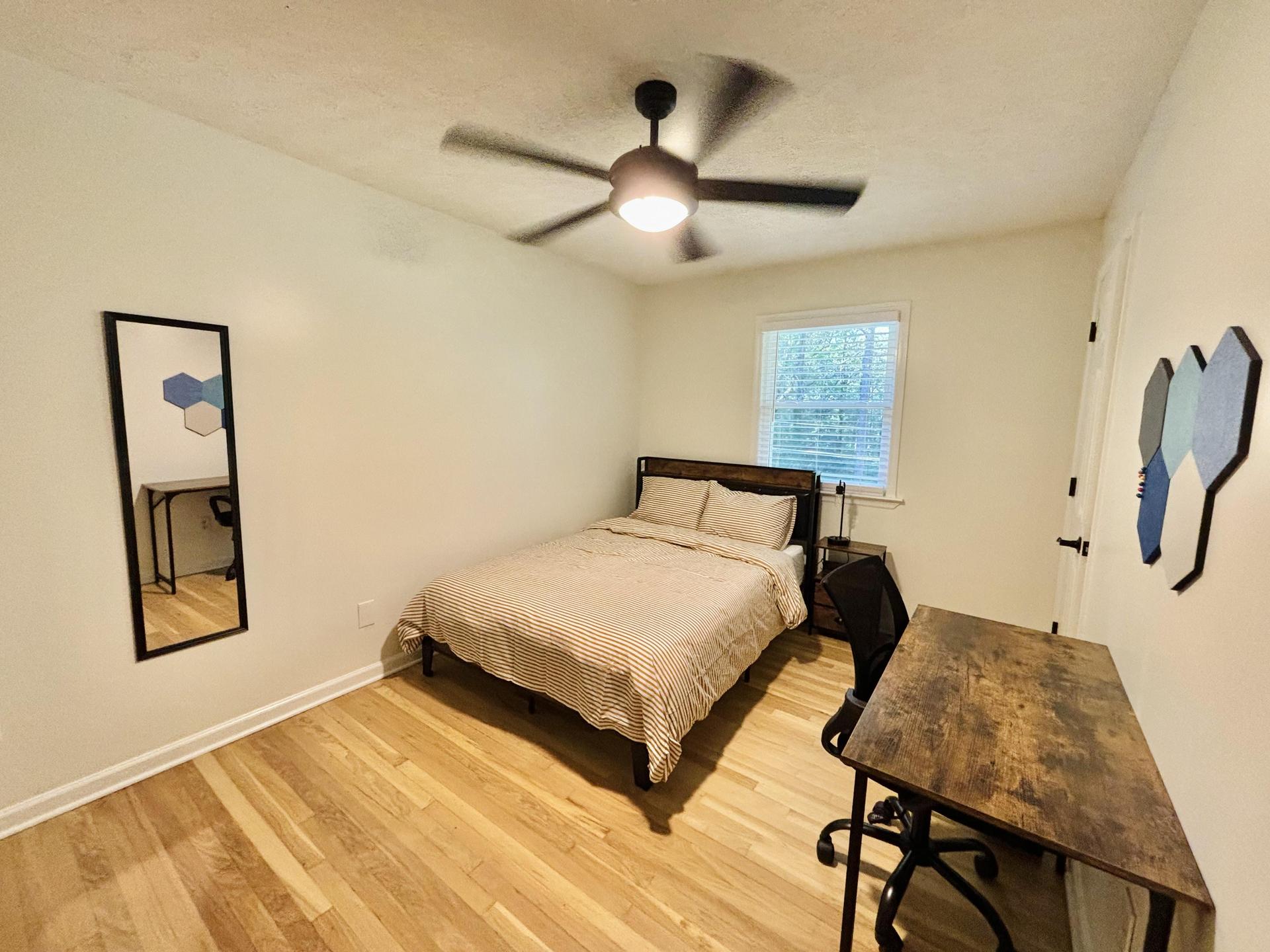 Spacious bedroom with full sized bed, mounted smart TV, desk & bulletin board, and full length mirror!