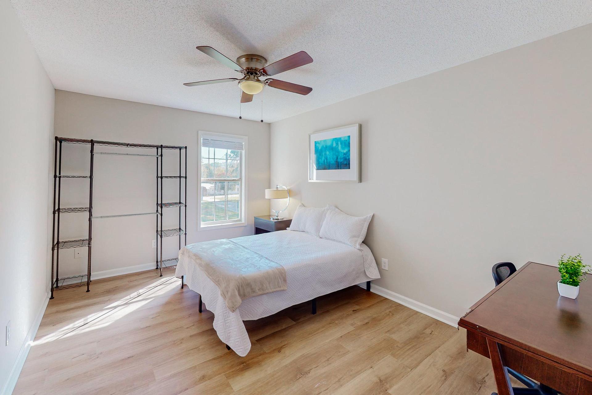 Private bedroom with Full size bed, nightstand, desk, ceiling fan and clothes rack.