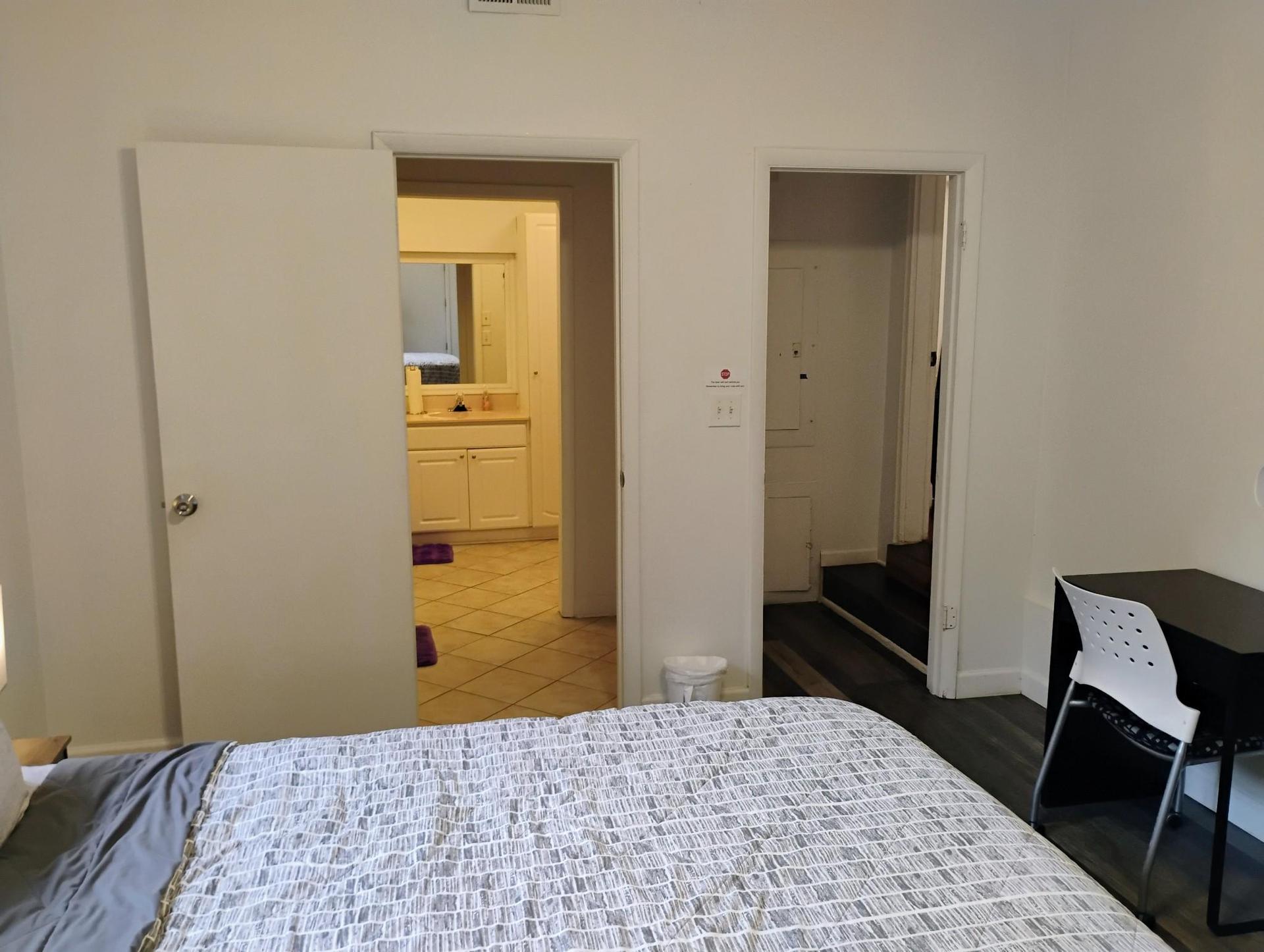 View of bedroom area into large private bathroom TV and dresser